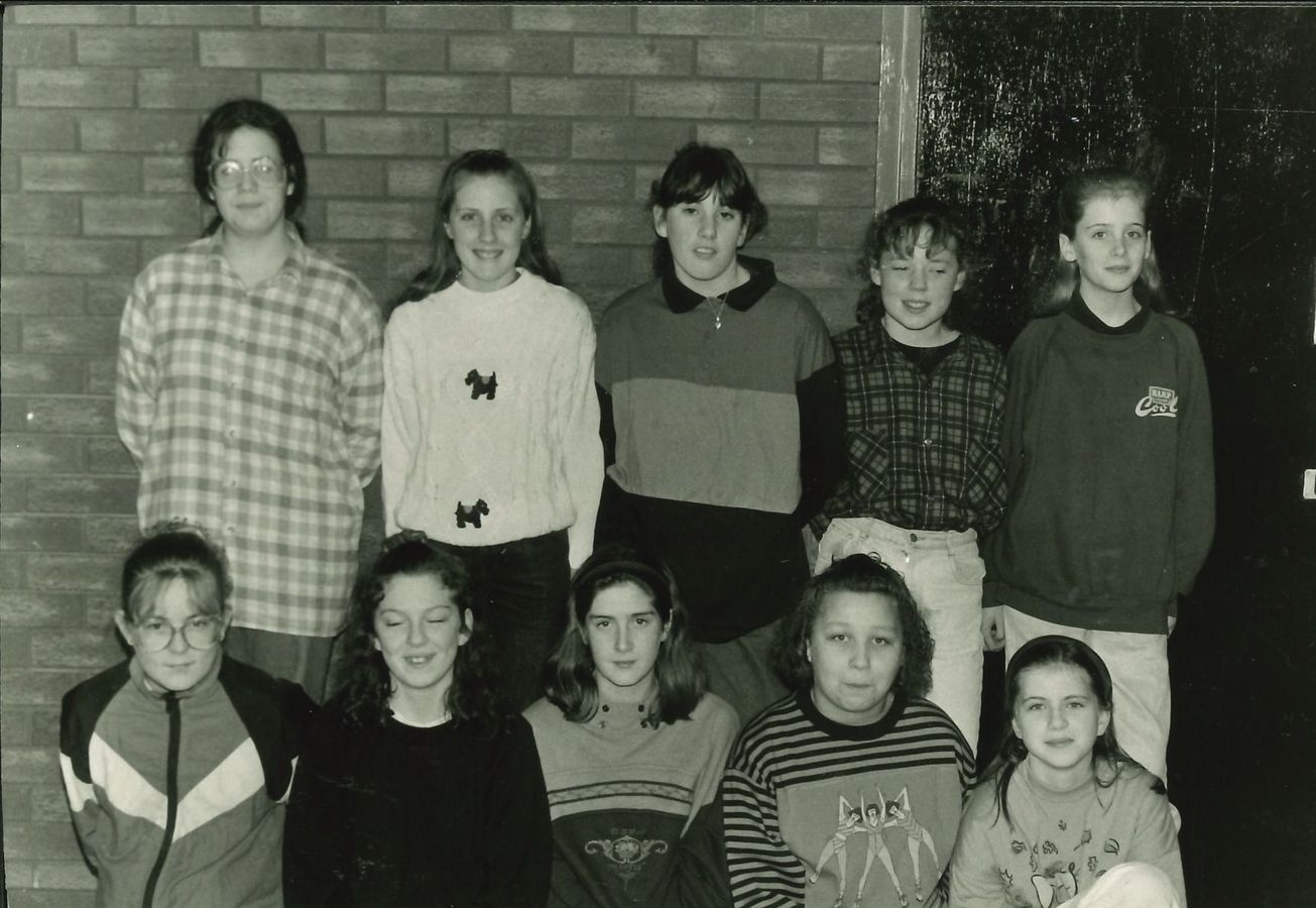 Ten club members posing in two rows against a brick wall